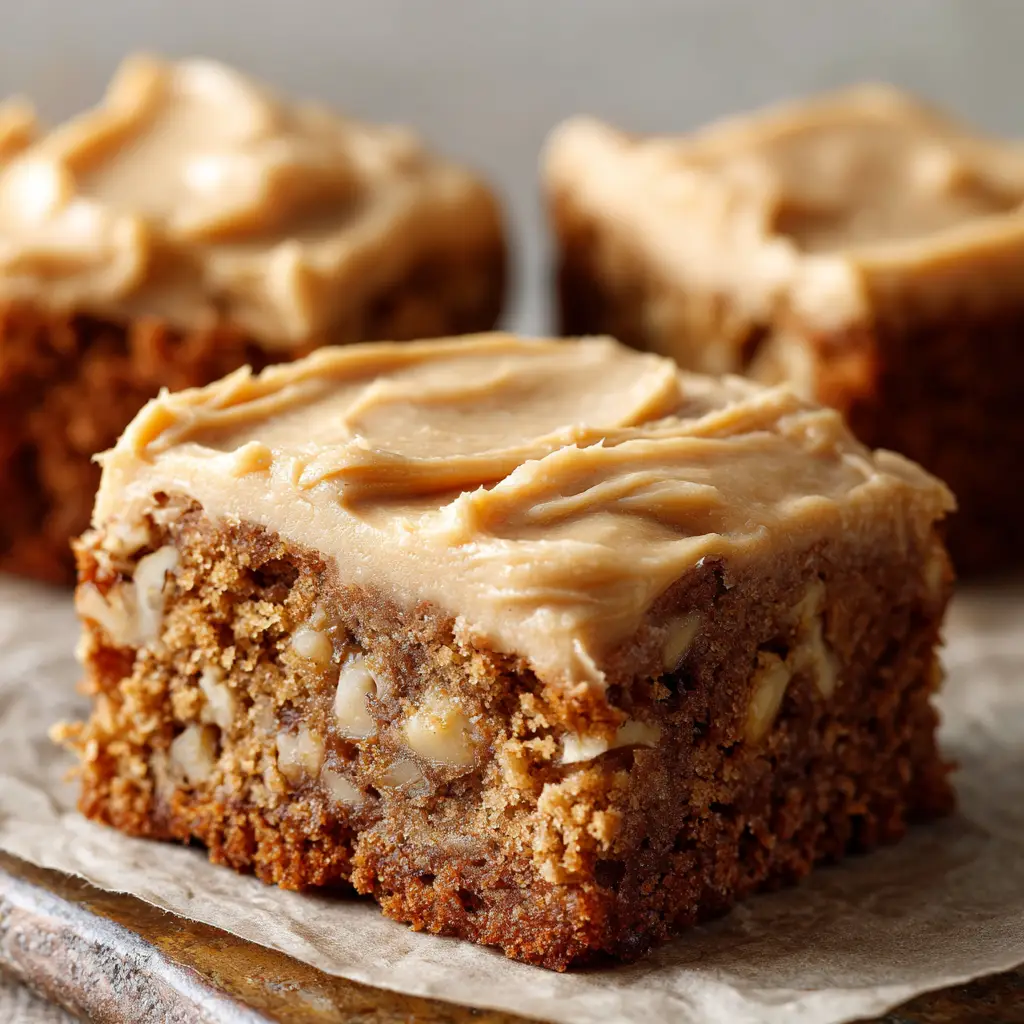 Close up macro shot of a thick banana bread blondie showing visible chunks of walnut and a luscious swirl of cream cheese frosting.