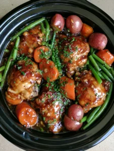 Top-down view of a black ceramic slow cooker filled with Slow Cooker Honey Garlic Chicken, featuring glazed thighs and thick carrot rounds.