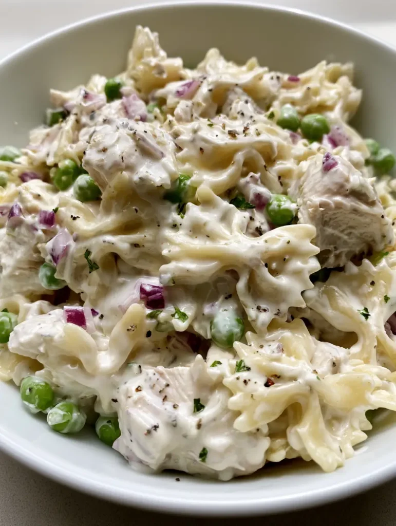 Creamy Chicken Pasta Salad with Farfalle and Sweet Peas 1 Creamy Chicken Pasta Salad with cracked black pepper and dried parsley visible on the surface.
