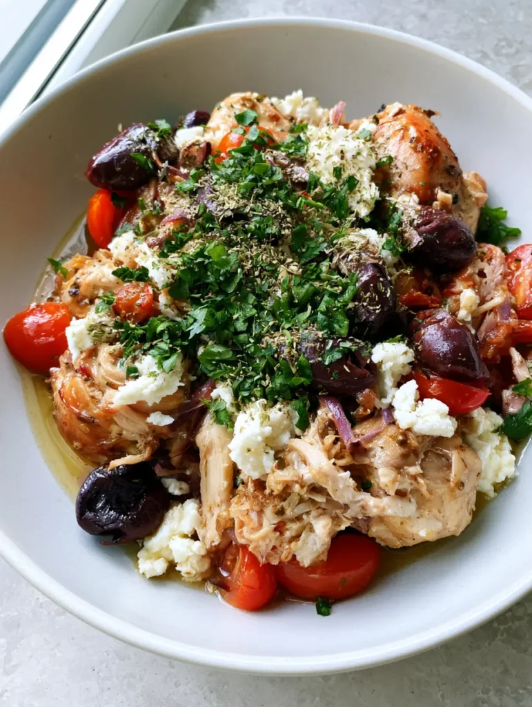 Close-up of Slow Cooker Greek Chicken garnished with fresh parsley, dried oregano, and crumbled feta.