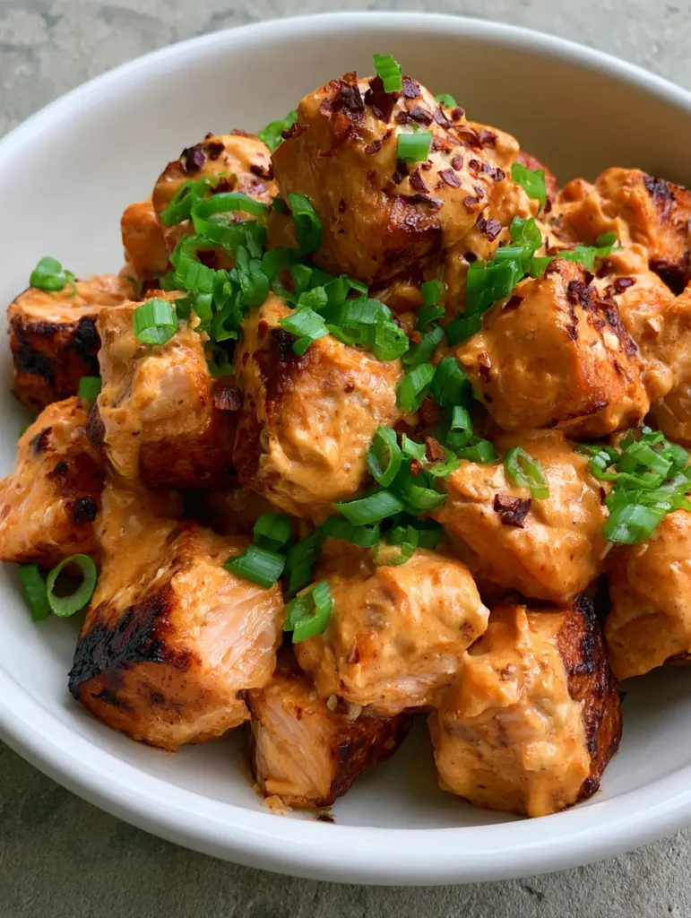 Bang Bang Salmon Bites: The Ultimate 20-Minute Crispy Appetizer 1 Overhead view of charred Bang Bang Salmon Bites in a ceramic bowl on a grey stone surface.