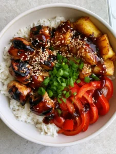 Close up of a Hawaiian Chicken Bowl showing the dark char on chicken breast cubes and thick glossy teriyaki glaze.
