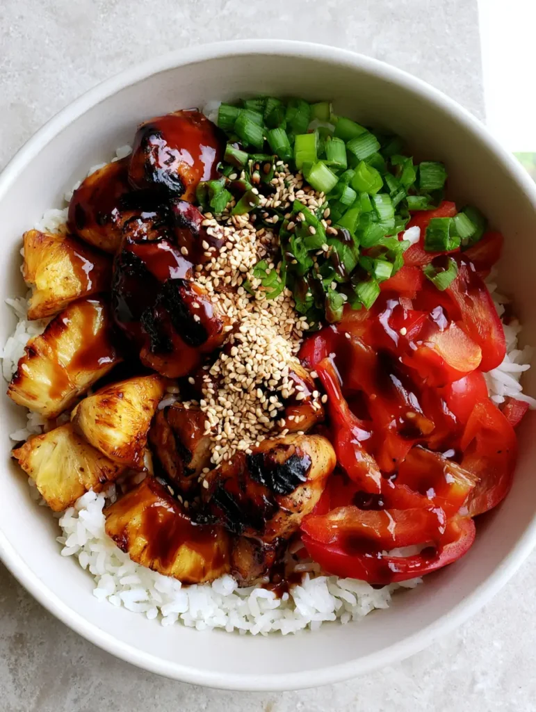 Hawaiian Chicken Bowl with Charred Pineapple and Teriyaki Glaze 1 Top-down view of a Hawaiian Chicken Bowl with vibrant green scallions and toasted white sesame seeds on a grey stone background.