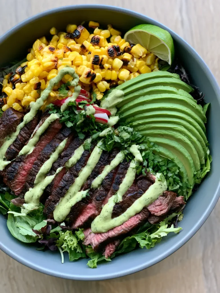 Top down shot of Steak and Avocado Bowl with rows of medium-rare steak, charred corn, and sliced avocado.