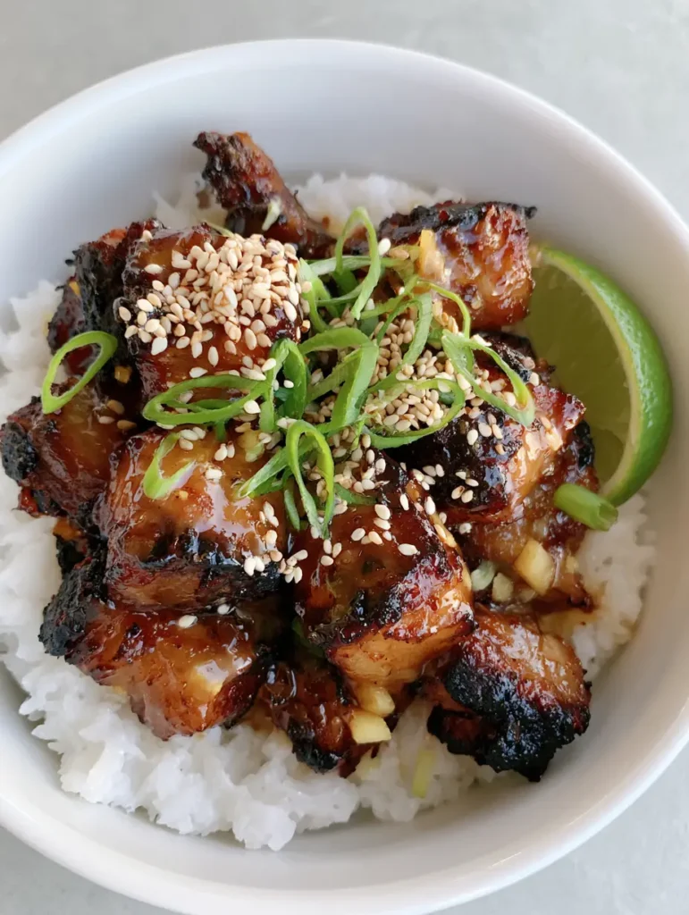 Top-down view of Ginger Lime Pork featuring charred pork edges, glossy glaze, scallions, and a lime wedge.