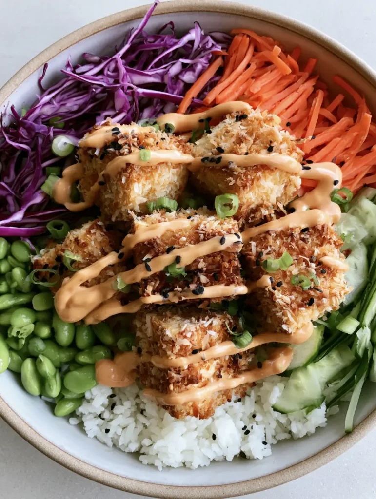 Close up shot of golden-brown coconut crusted tofu cubes arranged on a bed of jasmine rice with colorful vegetables.