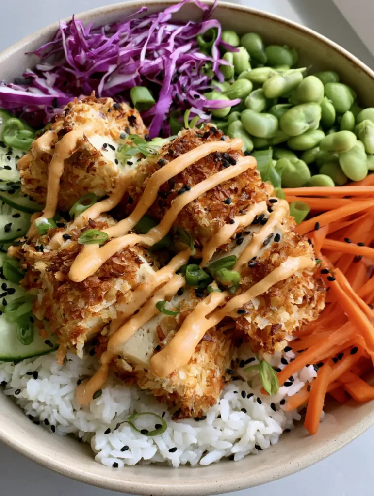 A complete Coconut Crusted Tofu Bowl featuring fresh julienned carrots, shredded cabbage, edamame, and cucumber.