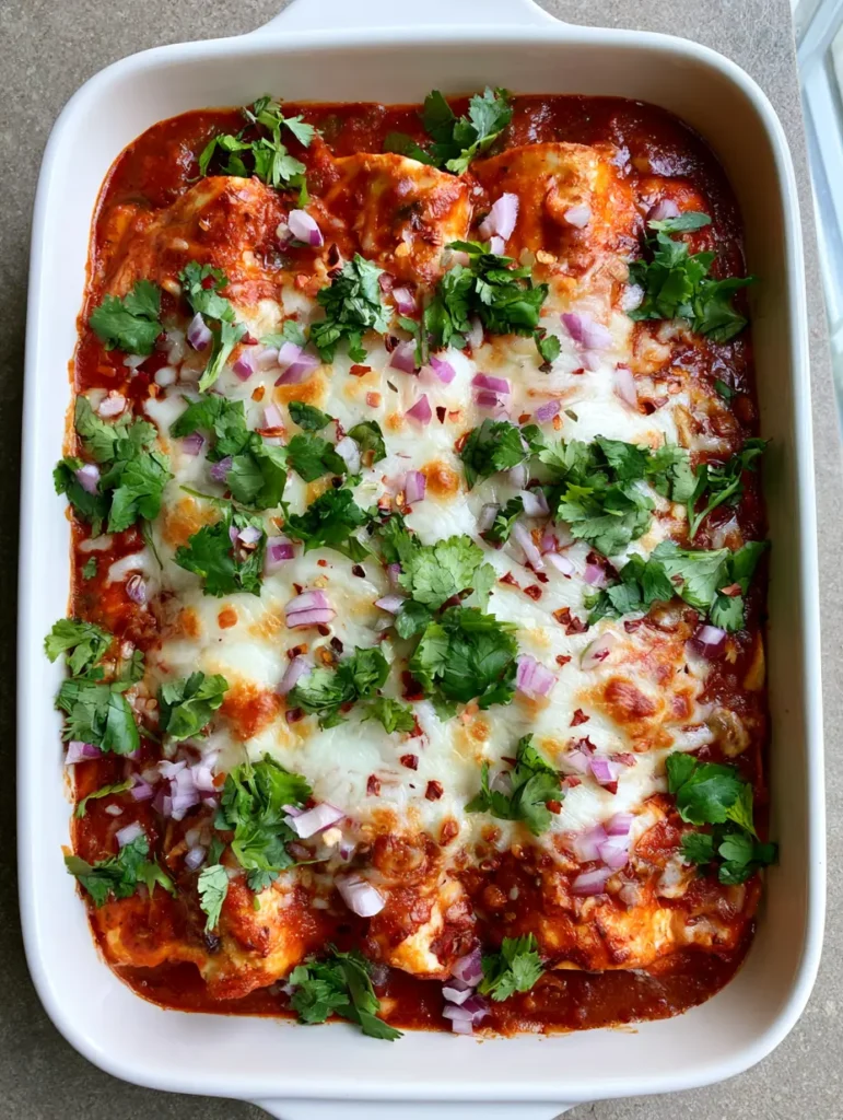 A smartphone photo showing the bubbly melted cheese and vibrant red sauce of High Protein Chicken Enchiladas in a white ceramic dish.