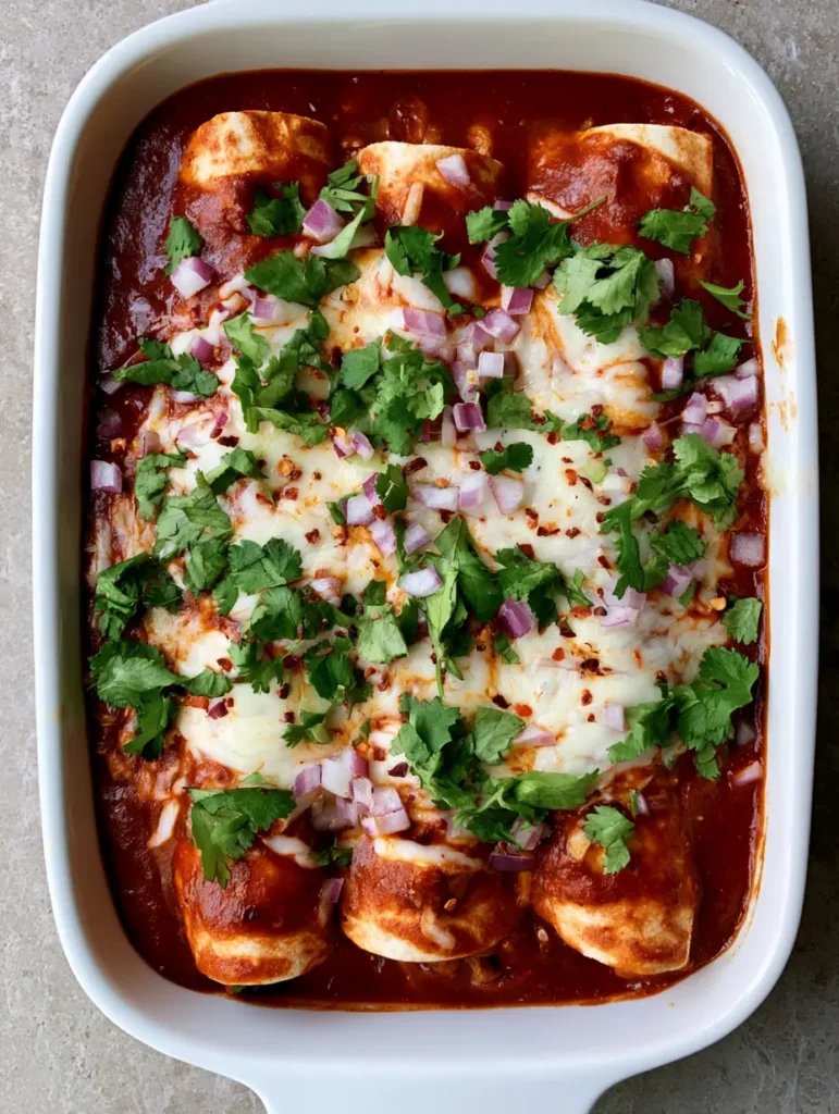 Close up of High Protein Chicken Enchiladas garnished with fresh cilantro, red pepper flakes, and finely diced red onion.