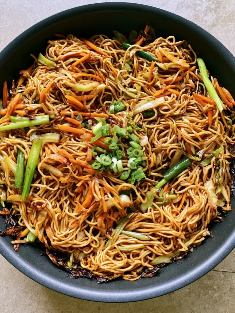 Stir-fried wheat noodles with julienned orange carrots and green cabbage in a black skillet. (Homemade Chow Mein Recipe)