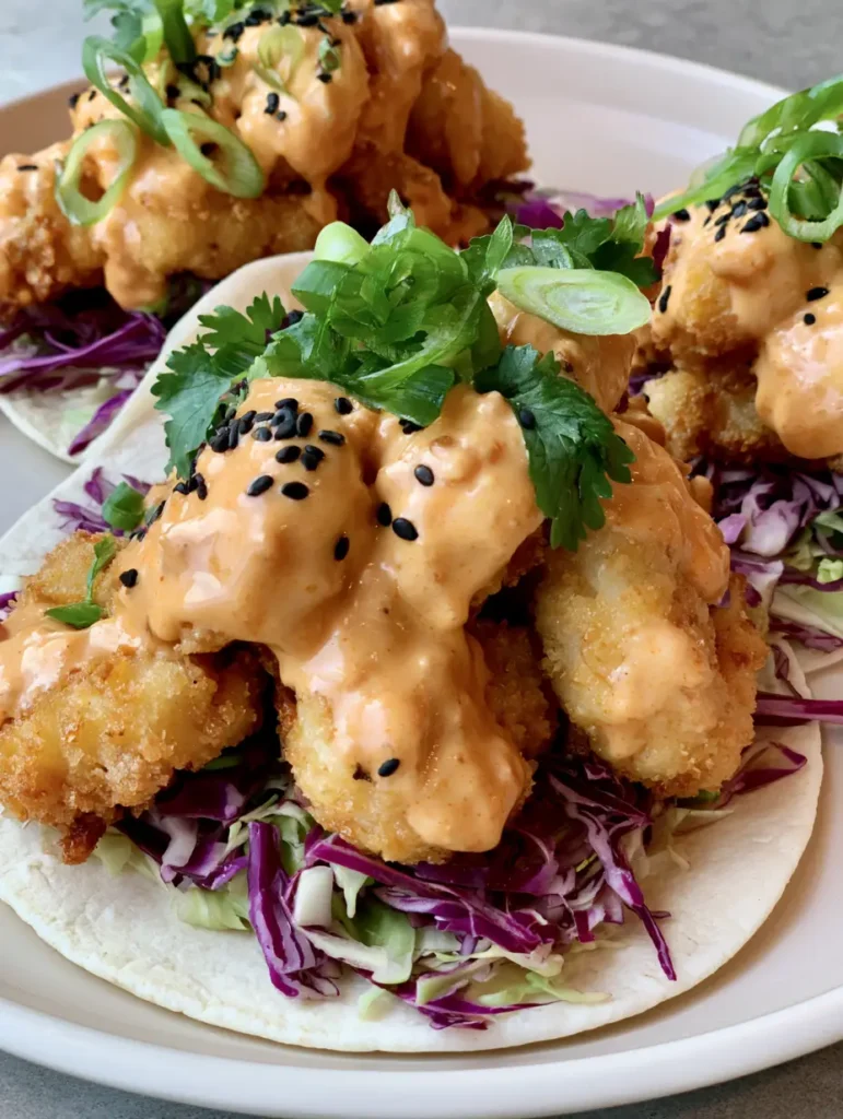 Home 8 Close up of street tacos with golden breaded shrimp, pale orange spicy sauce, and shredded purple cabbage. (Bang Bang Shrimp Tacos)
