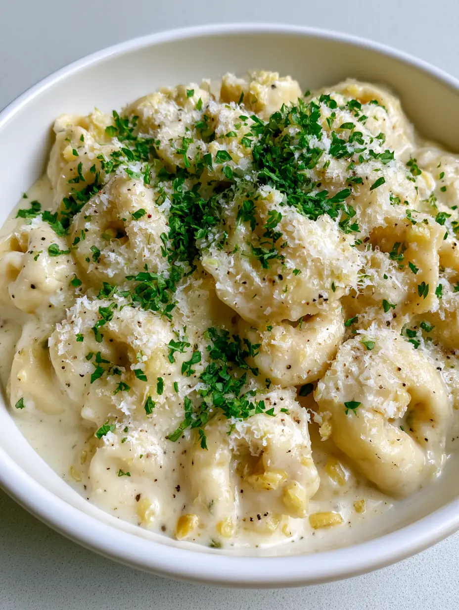Shallow white ceramic bowl filled with plump cheese-filled Creamy Garlic Butter Tortellini garnished with snowy parmesan.