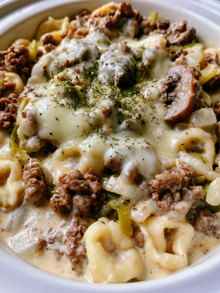 Crock Pot Cheesesteak Tortellini: Creamy Philly-Style Comfort 2 Close-up of Crock Pot Cheesesteak Tortellini showing browned ground beef, soft green peppers, and melted mozzarella patches garnished with parsley.