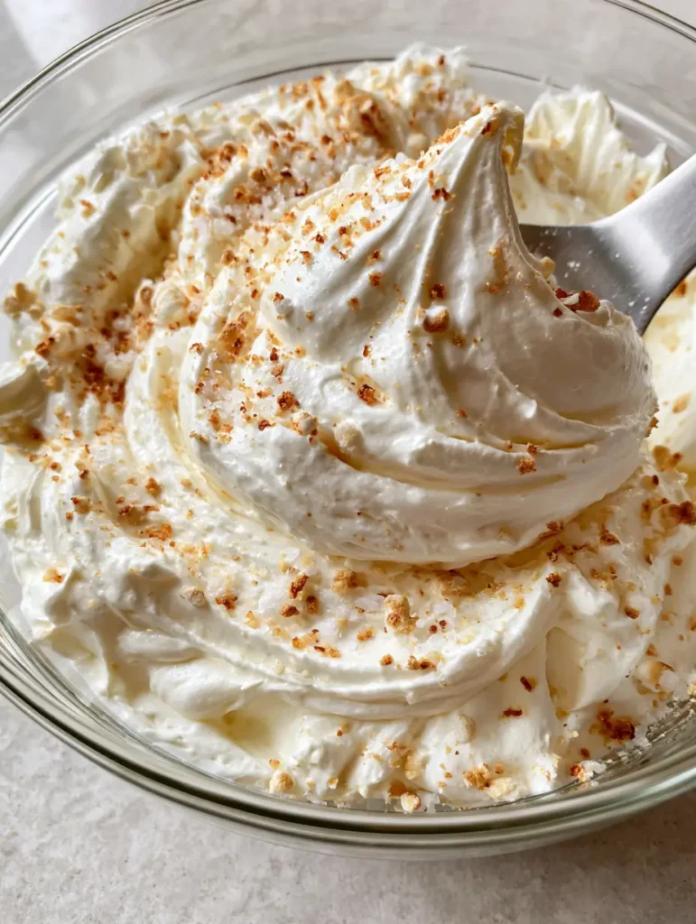 High-angle shot of glossy white Marshmallow Buttercream Frosting with a silver spatula swirl.