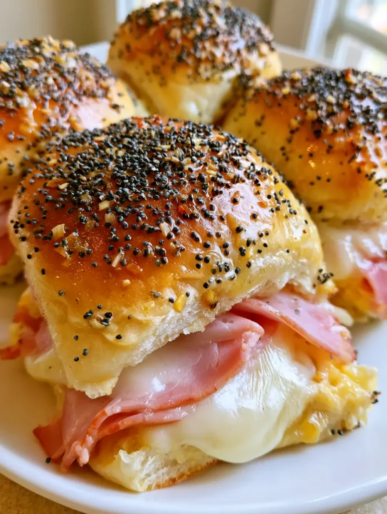 A white plate with several Hawaiian Ham and Cheese Sliders showing the layers of smoked ham and melted Swiss cheese.