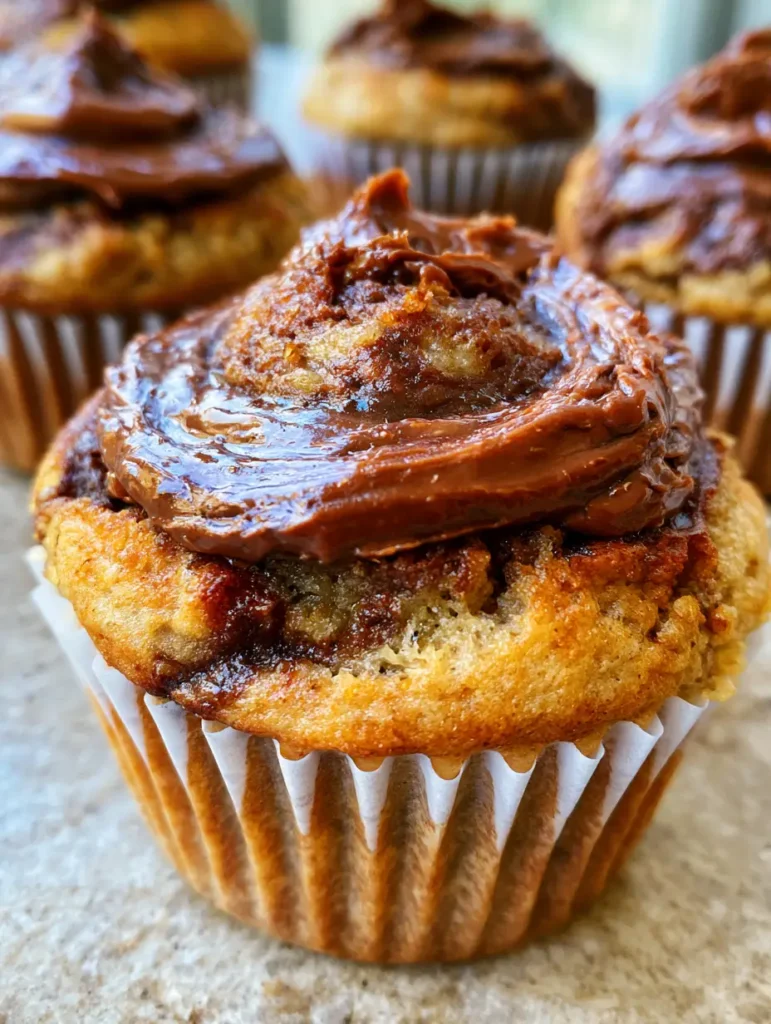 Nutella Banana Swirl Muffins: The Ultimate Bakery-Style Recipe 1 Nutella Banana Swirl Muffins sitting on a light-colored stone countertop under soft natural daylight.