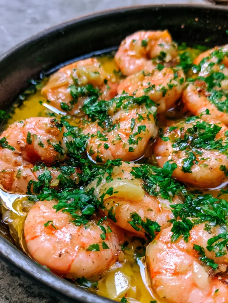 Garlic Butter Shrimp arranged in a shallow dark cast iron skillet with black pepper specks.