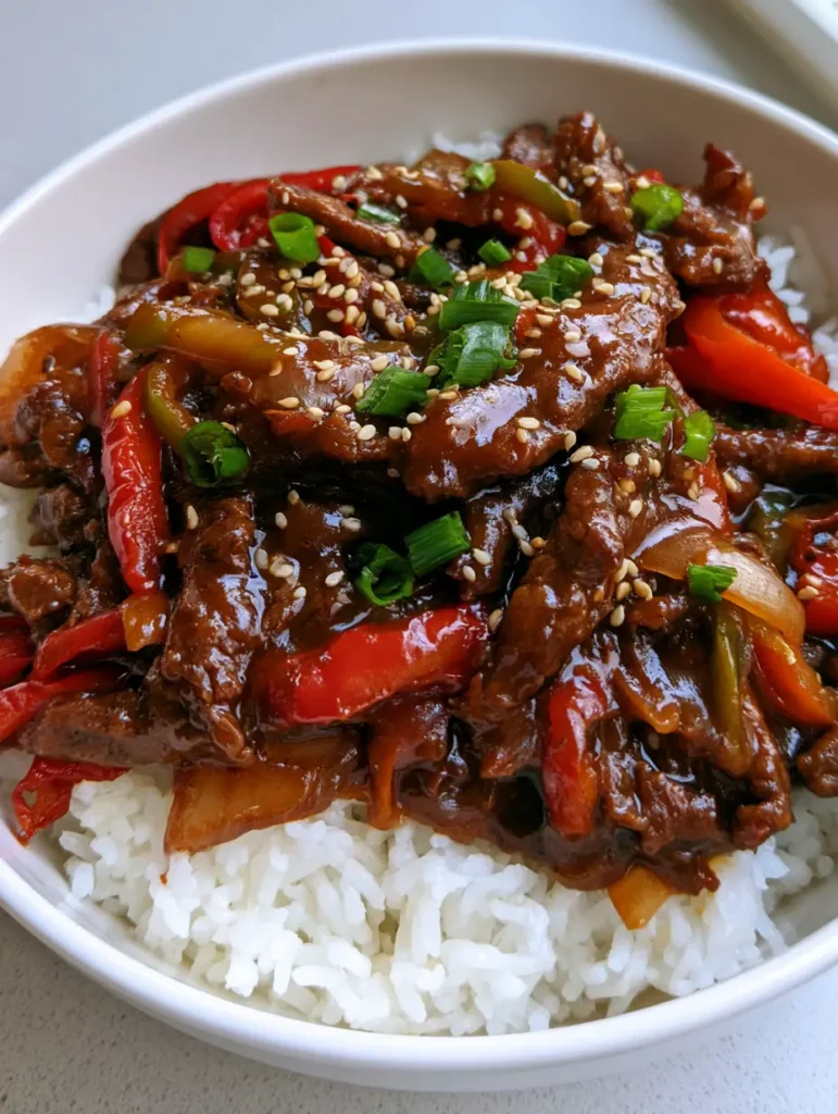 Handheld photo of Slow Cooker Pepper Steak in a white bowl with sesame seeds and scallions.