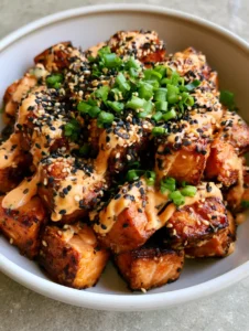 A close-up shot of crispy cubed Bang Bang Salmon Bites piled in a ceramic bowl on a gray stone countertop.