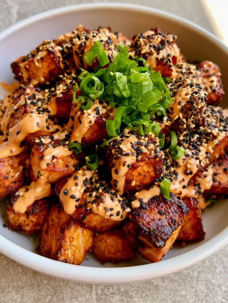 Macro view of Bang Bang Salmon Bites with a thick glossy pale-orange sauce drizzle and toasted black and white sesame seeds.
